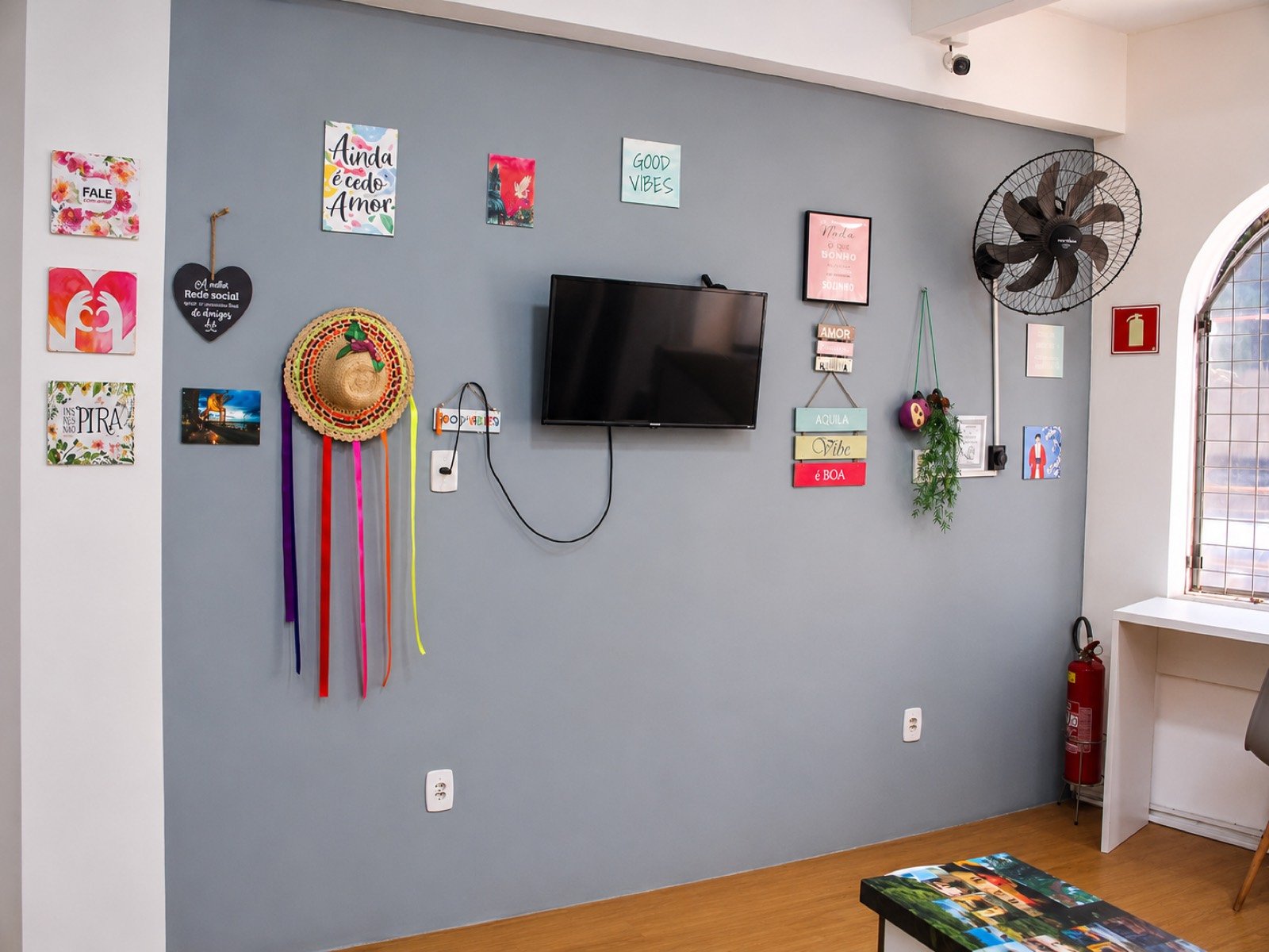 Sala de convivência do Cunhatã Hostel com TV, chapéu e mural de recados